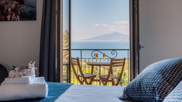 A bedroom with a bed, a balcony with a table and chairs, and a painting on the wall. - Relais S. Francesco  (Sorrento)