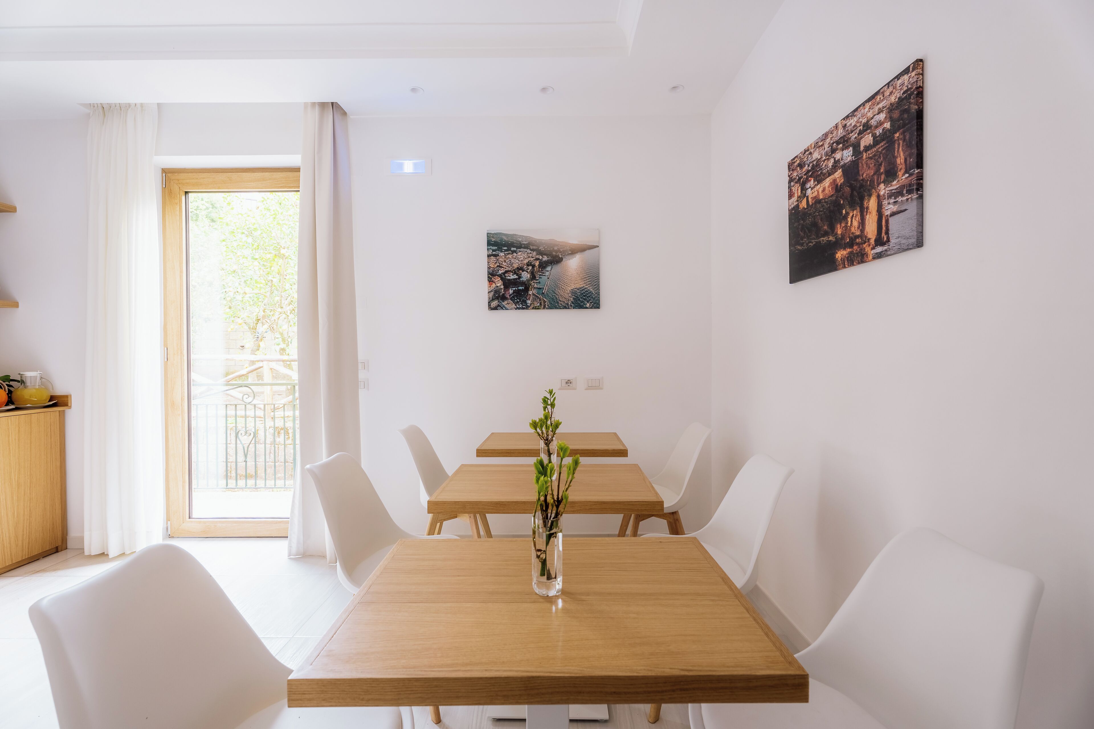 A dining area with a wooden table, white chairs, and a vase with greenery.