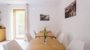 A dining area with a wooden table, white chairs, and a vase with greenery.