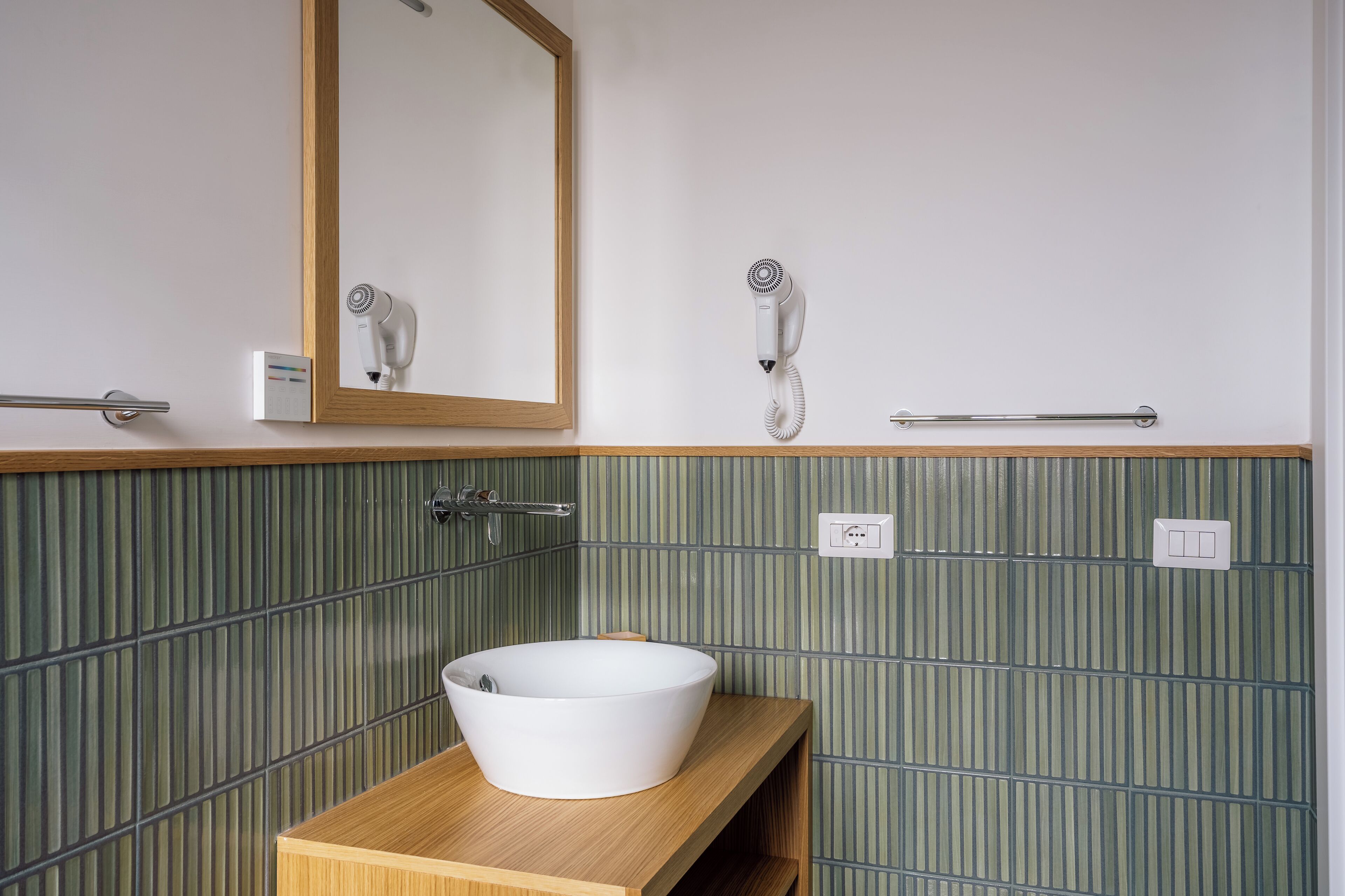 A bathroom with a wooden vanity, a white sink, a mirror, a hairdryer, and a towel rack.