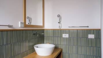 A bathroom with a wooden vanity, a white sink, a mirror, a hairdryer, and a towel rack.