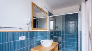 A bathroom with a wooden vanity, a white sink, a mirror, and a glass shower enclosure. - Relais S. Francesco  (Sorrento)
