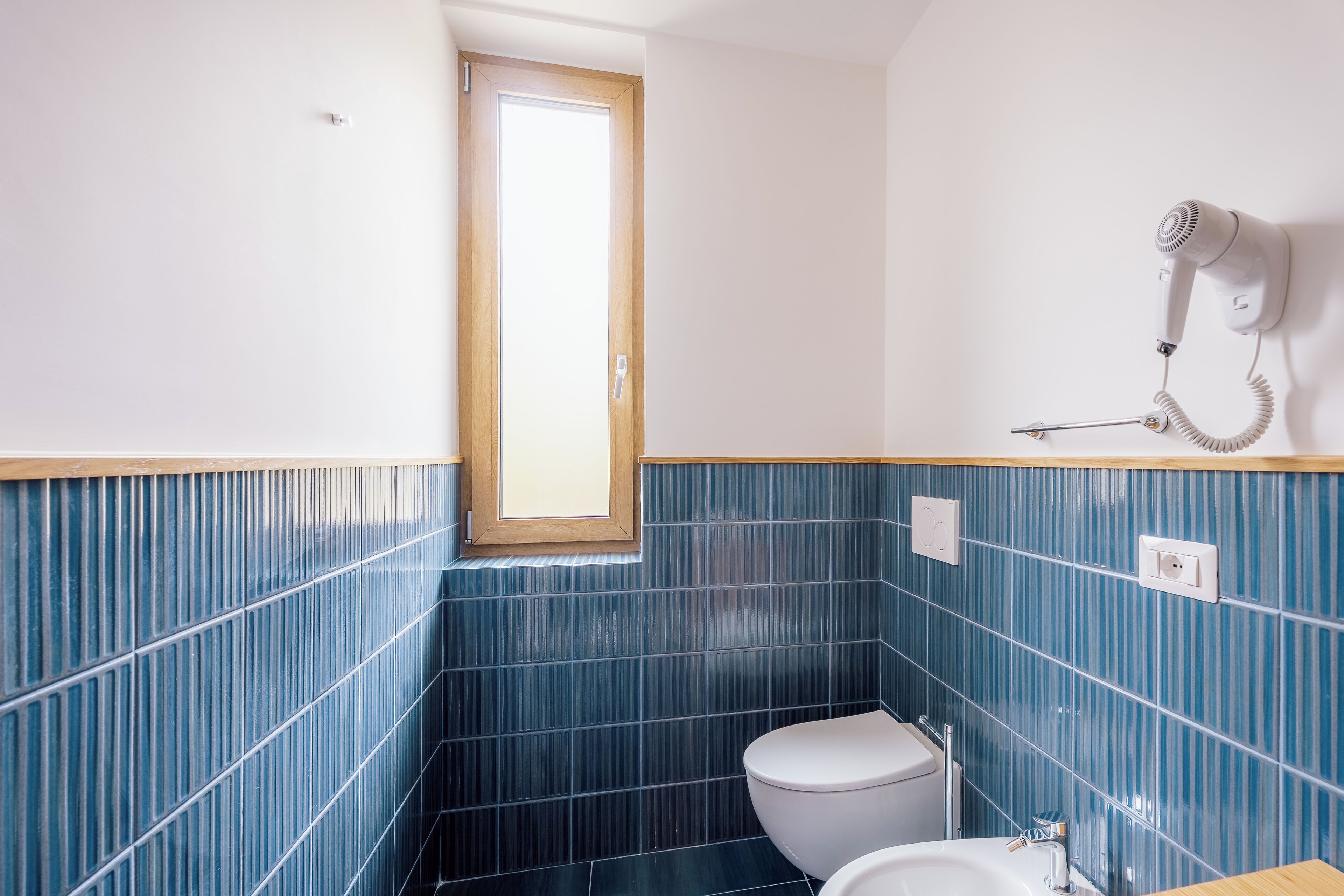 Un baño con inodoro blanco, lavamanos y un secador de pelo montado en la pared.