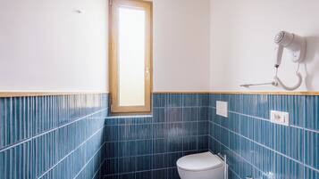 Un baño con inodoro blanco, lavamanos y un secador de pelo montado en la pared.