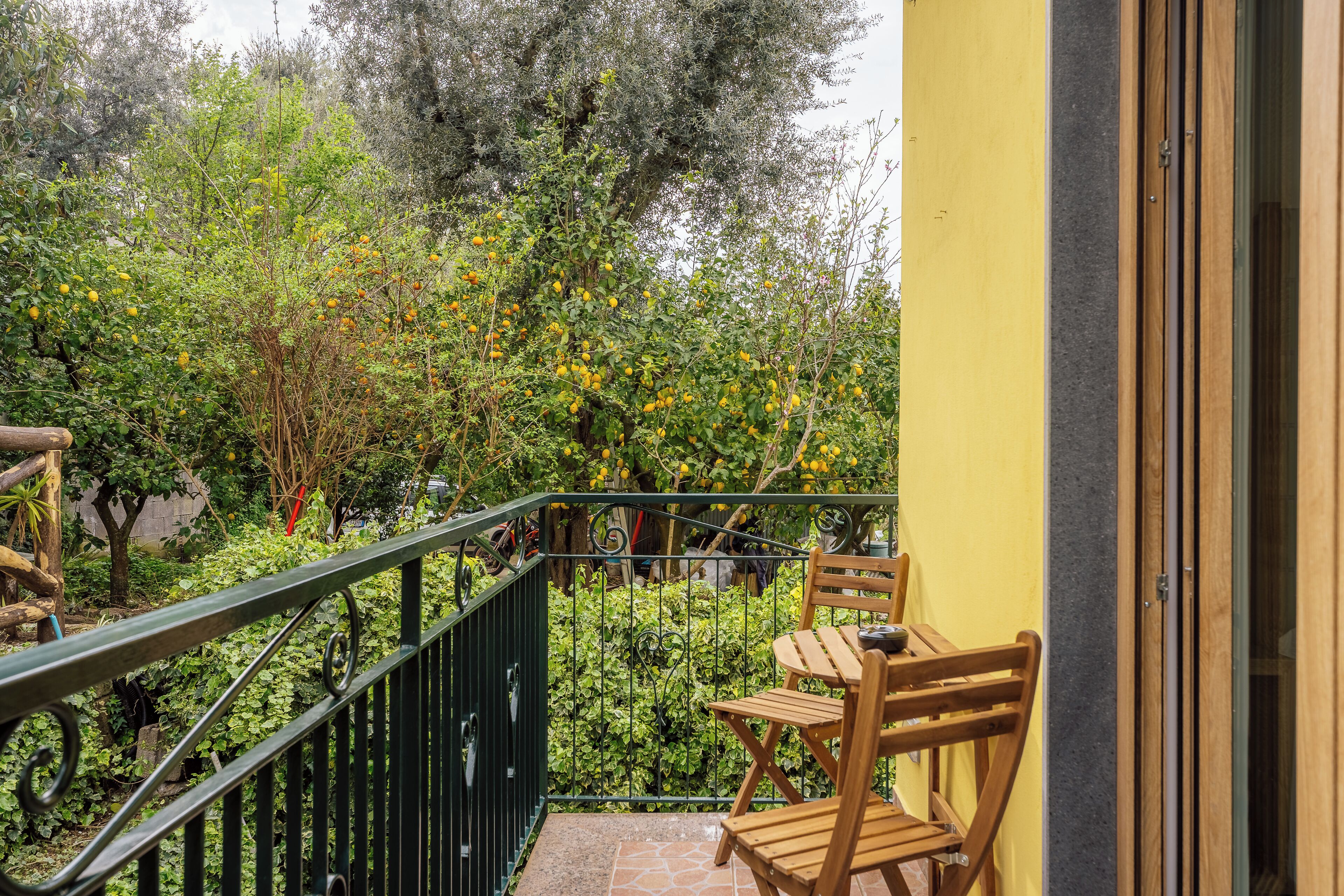 A balcony with a wooden chair, a metal railing, and a yellow wall.