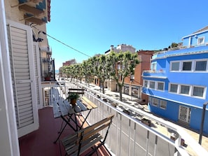A balcony with a wooden table and benches, overlooking a street with trees and buildings.