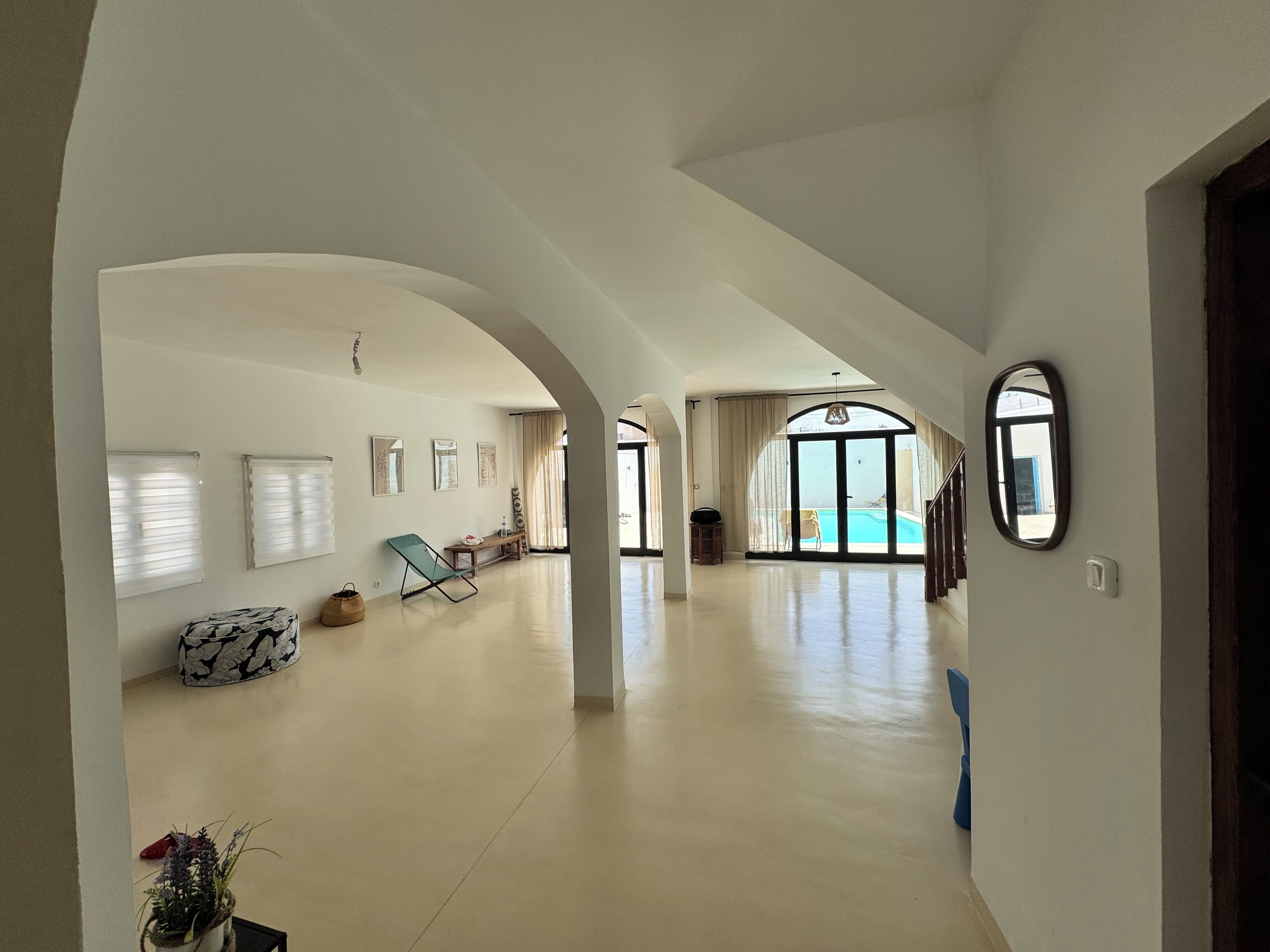 Um corredor amplo com vista para a piscina, paredes brancas e uma grande porta em arco.