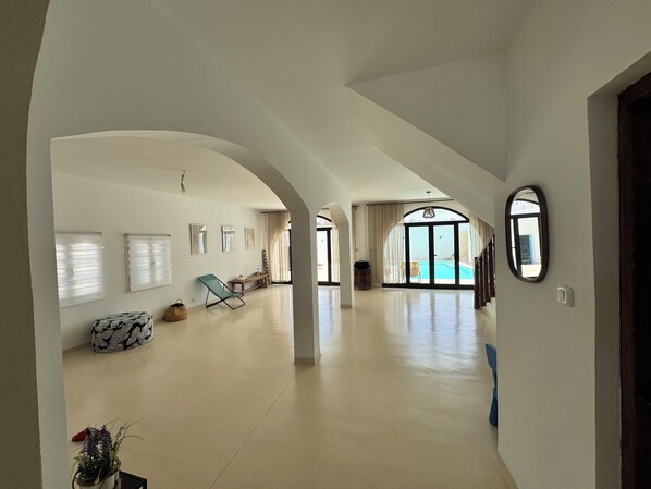 A spacious hallway with a pool view, white walls, and a large arched doorway.