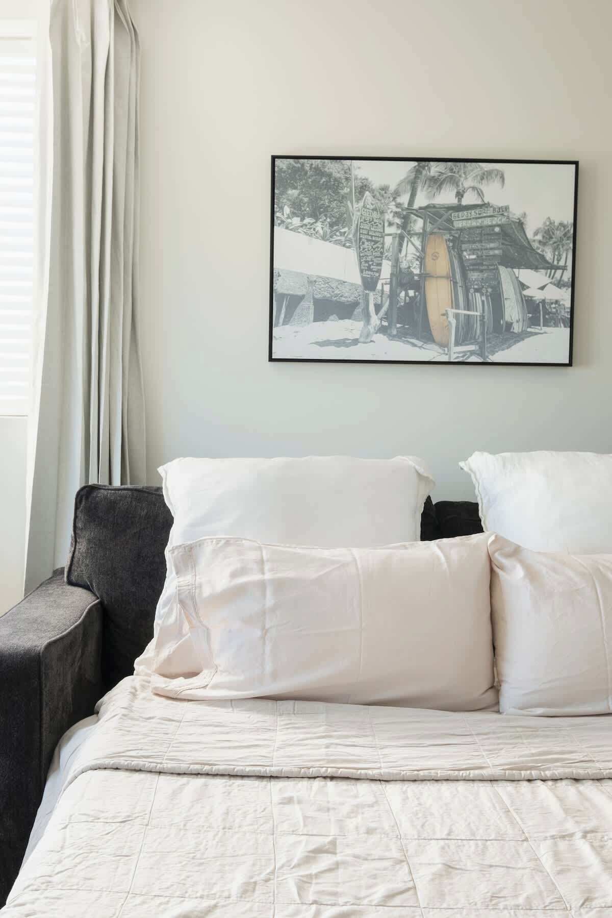 Una cama con ropa de cama y almohadas blancas, un sillón gris y una fotografía en blanco y negro en la pared.