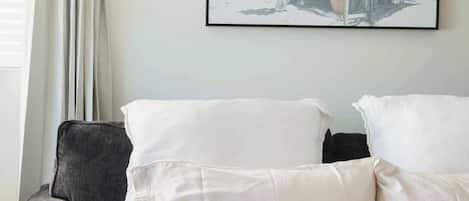 Una cama con ropa de cama y almohadas blancas, un sillón gris y una fotografía en blanco y negro en la pared.