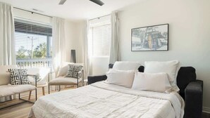 Un dormitorio con una cama grande, dos sillas, un ventilador de techo y una ventana con persianas.