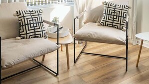 Una sala moderna con dos sillones, una mesita redonda y vistas a un balcón con barandilla.