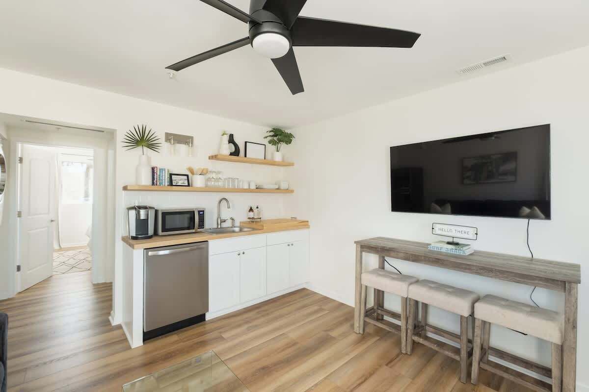 Une cuisine moderne avec des armoires blanches, un plan de travail en bois, un four à micro-ondes encastré et un ventilateur de plafond.
