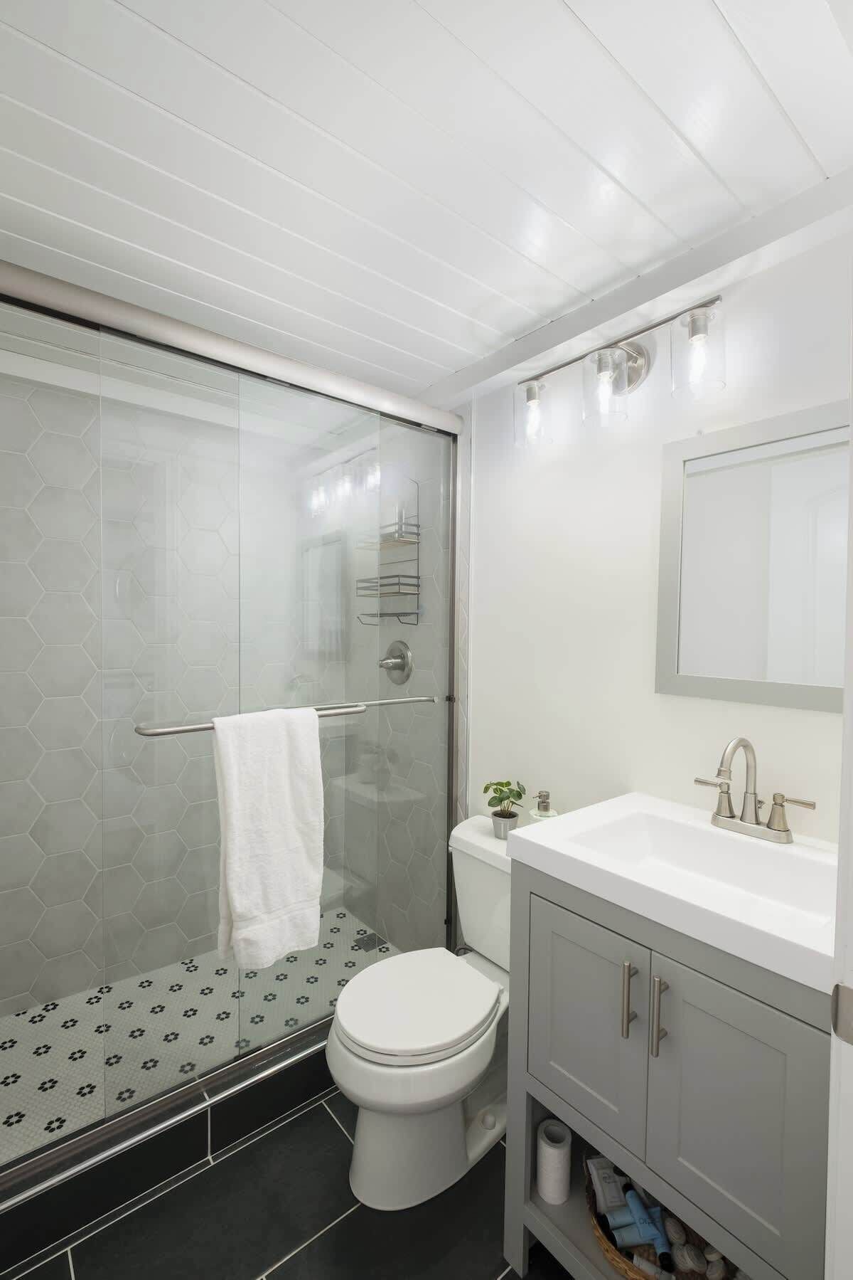 Een moderne badkamer met een glazen douchecabine, een wit toilet en een wastafelmeubel met wastafel en spiegel.
