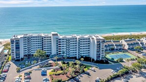 A multi-story hotel with a pool and tennis court, located near a beach and ocean.