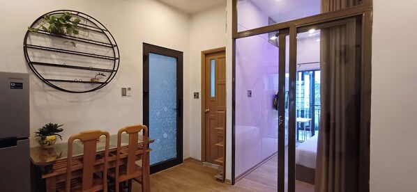 A hallway with a dining area featuring a wooden table and chairs, a wall-mounted plant shelf, and a sliding glass door leading to a balcony.