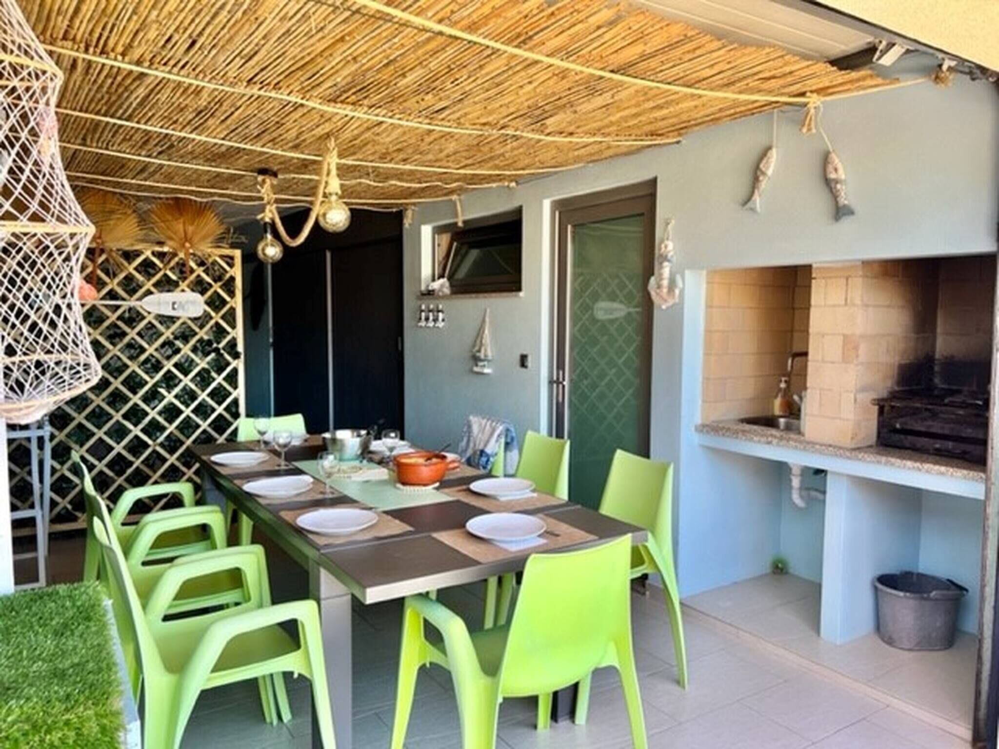 A dining area with a long table, green chairs, a thatched ceiling, and a built-in grill.