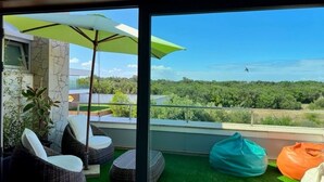 Un balcon avec des sièges d’extérieur, un parasol vert et une vue sur une zone boisée.