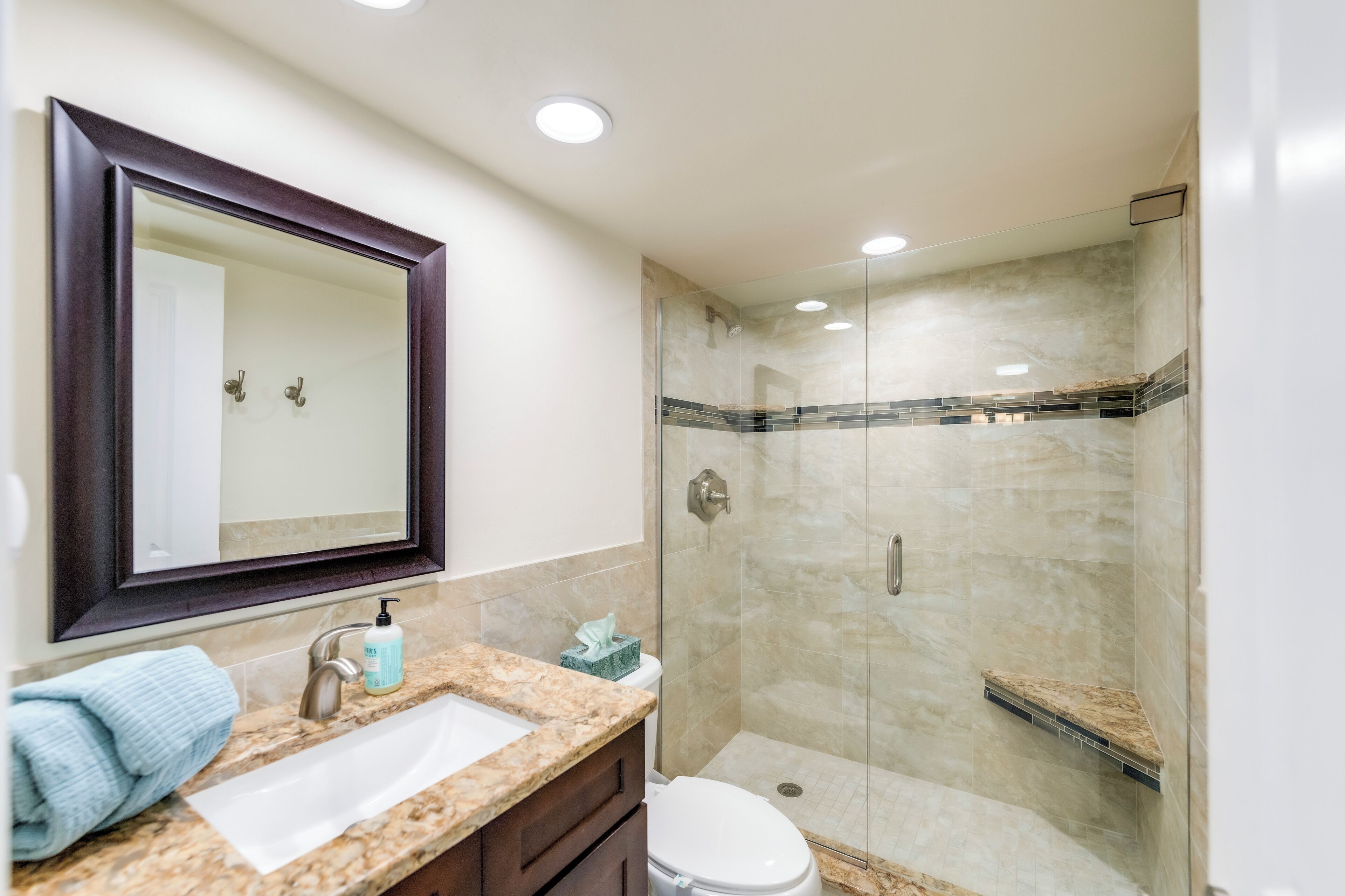 A bathroom with a marble sink, a mirror, a toilet, and a glass-enclosed shower.