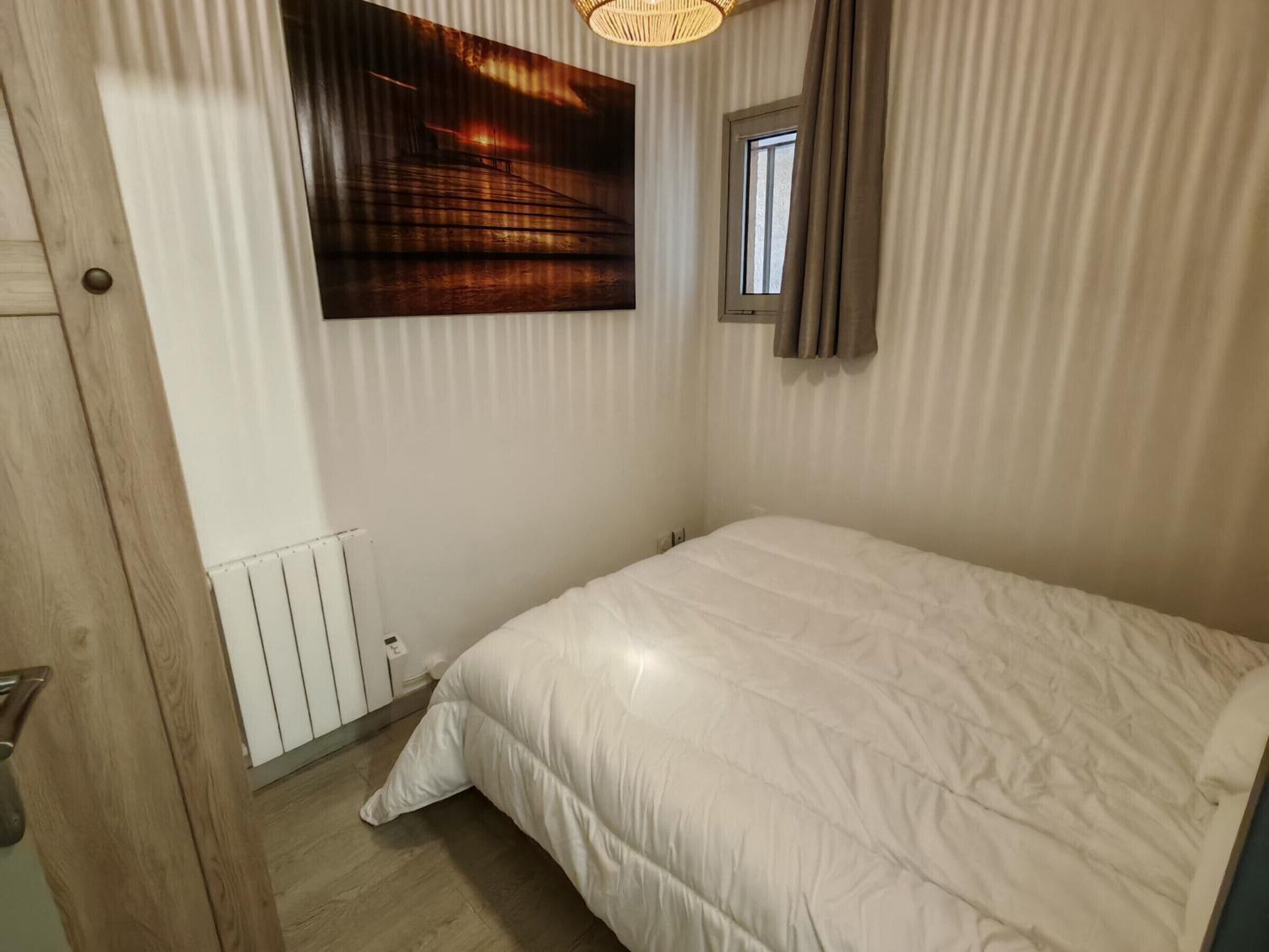 Ein Schlafzimmer mit einem Bett, einem Fenster, einer Heizung und einem Wandbild.