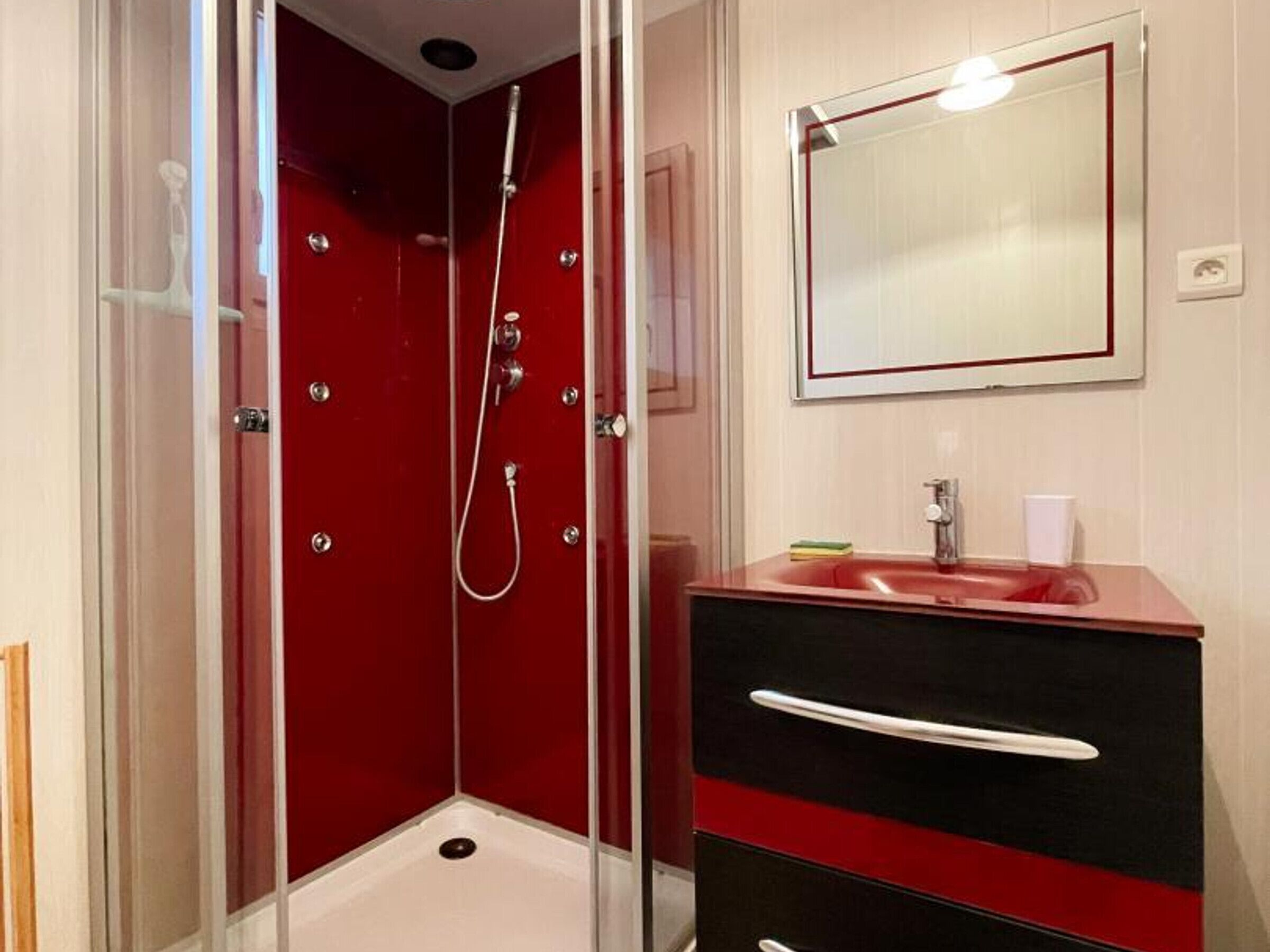Une salle de bain avec un receveur de douche rouge, un lavabo avec un miroir et un meuble-lavabo noir et rouge.
