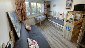 A cozy room with a bed, a small table, a TV, and a wooden playpen. - Cozy T2 in the heart of Le Lioran (Le Lioran)