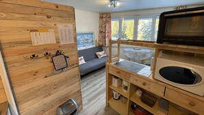A compact kitchen with wooden cabinetry, a microwave, and a sink. There's a small dining table and a sofa in the adjacent living area. - Cozy T2 in the heart of Le Lioran (Le Lioran)