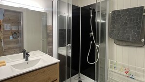 A modern bathroom with a glass-enclosed shower, a white sink, and a wooden vanity. - Cozy T2 in the heart of Le Lioran (Le Lioran)