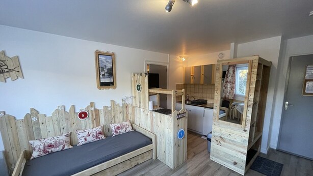 A compact room with a wooden bed, a small kitchenette, and a bathroom. - Cozy T2 in the heart of Le Lioran (Le Lioran)