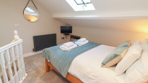 Ein Schlafzimmer mit Dachfenster, einem Bett mit Kissen, einem Fernseher und einem Spiegel.
