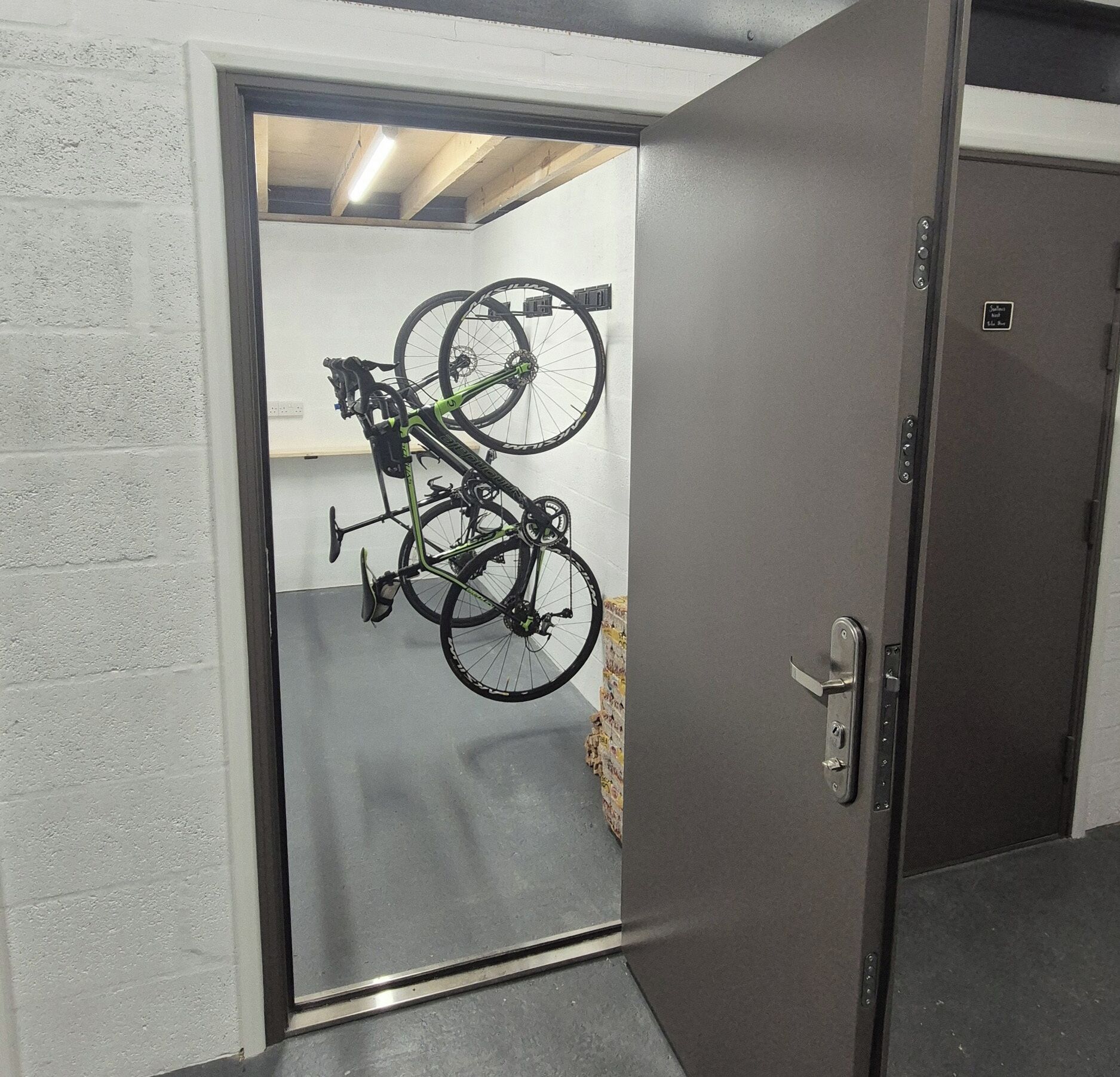 A door with a bicycle rack mounted on the wall, a door handle, and a small sign on the door.