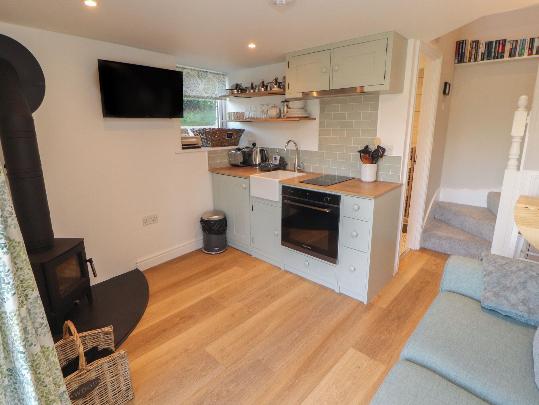 A compact kitchen with a built-in oven, a TV mounted above the counter, and a small trash bin.