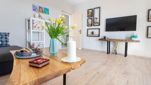 A modern living room with a wooden coffee table, a vase with flowers, a white candle, and a flat-screen TV mounted on the wall.