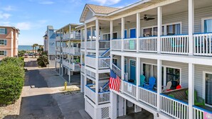 A beachfront hotel with multiple balconies, outdoor seating, and an American flag. - Tybee Condo | Ocean View Porch + Walk to Fun (Tybee Island)