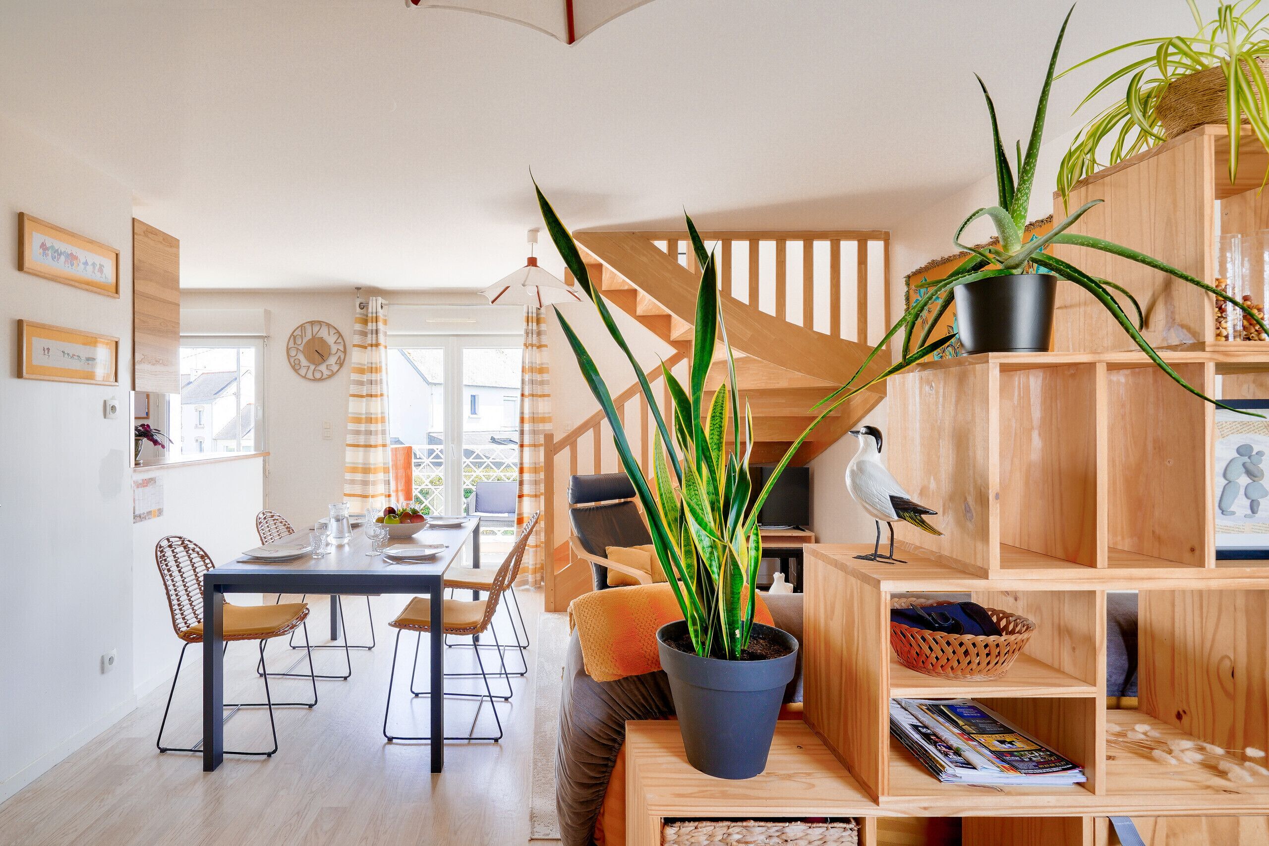 A modern living room with a dining area, wooden furniture, and potted plants.