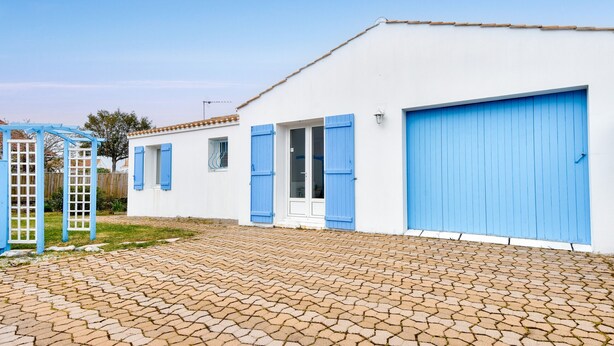 Un bâtiment blanc avec des volets bleus et un grand portail de garage.