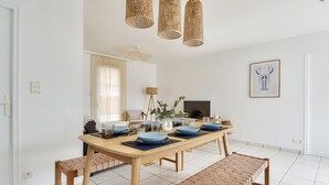 Un espace repas avec une longue table en bois, des assiettes bleues et des luminaires en fibres tressées.