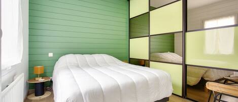 A room with a bed, a small table with a lamp, and a window.
