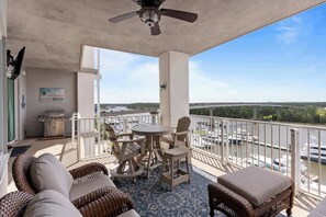 Ein Balkon mit Korbmöbeln, Deckenventilator und Blick auf Boote und Grünflächen.