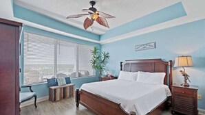 Ein Schlafzimmer mit einem Holzbett, einem Deckenventilator, einem Fenster mit Jalousien, einem Nachttisch und einem Beistelltisch.