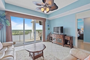 A spacious living room with a balcony, a ceiling fan, a television, and a wooden cabinet.