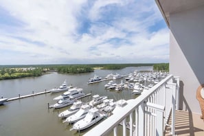 A marina with numerous yachts docked, a clear sky, and a view of the surrounding greenery.