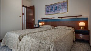 Ein Hotelzimmer mit zwei Betten, einem Holzkopfteil, Nachttischlampen, einem Bild an der Wand und einer Tür.