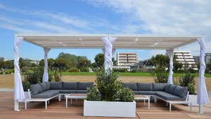 Ein Sitzbereich im Freien mit einem überdachten Pergola, einem Ecksofa und einem Pflanzgefäß mit Grünpflanzen.