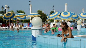 A swimming pool with multiple people, surrounded by sun umbrellas and lounge chairs.