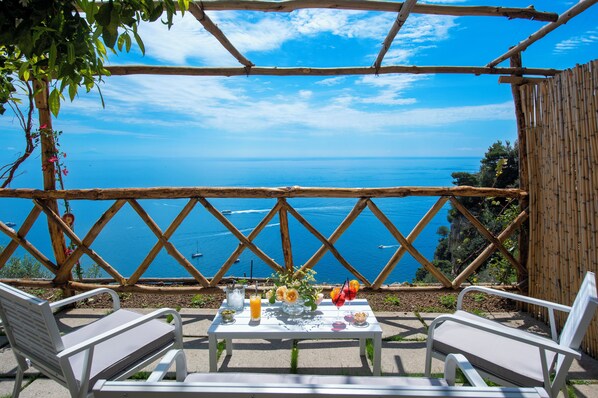 A table with drinks and flowers, two white chairs, and a view of the sea. - Villa Briganti Positano (Positano)