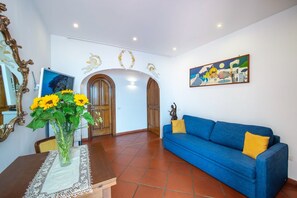 A living room with a blue sofa, a vase with yellow flowers, and a painting on the wall. - Villa Briganti Positano (Positano)