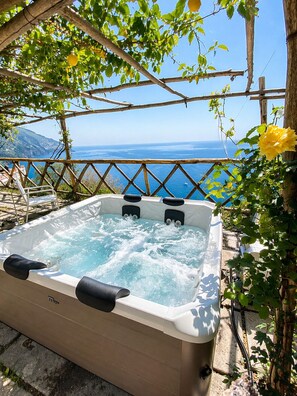 Un jacuzzi con vista al mar, rodeado de vegetación y una pérgola de madera.