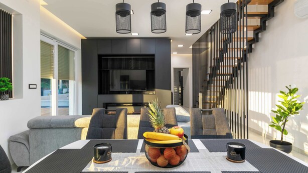 A modern living room with a sofa, a dining table with a fruit bowl, and a staircase. - Villa Eva with pool near Medulin (Ližnjan)