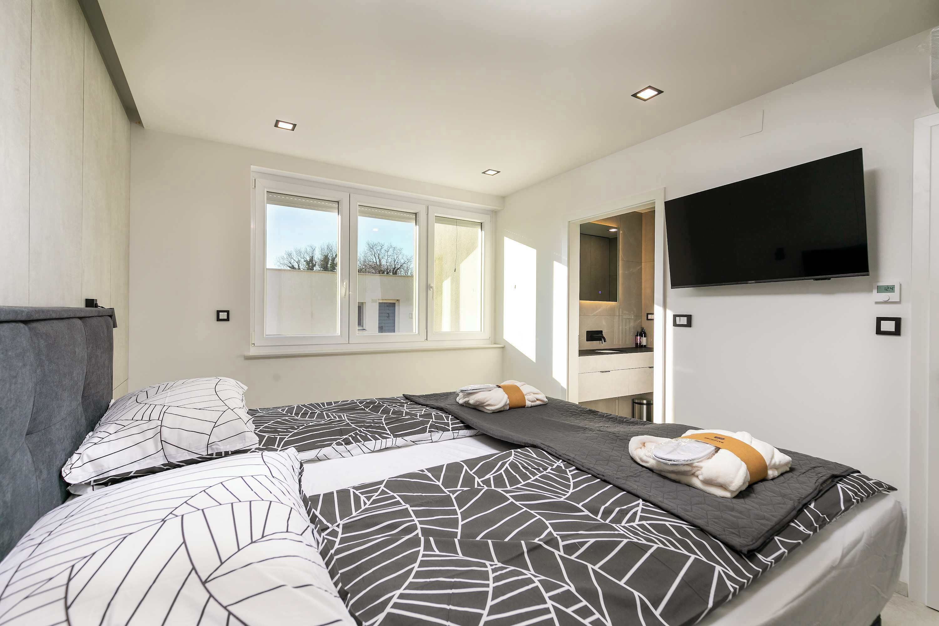Une chambre d’hôtel moderne dotée d’un grand lit, d’une télévision à écran plat, d’une fenêtre et d’une salle de bain avec un miroir.